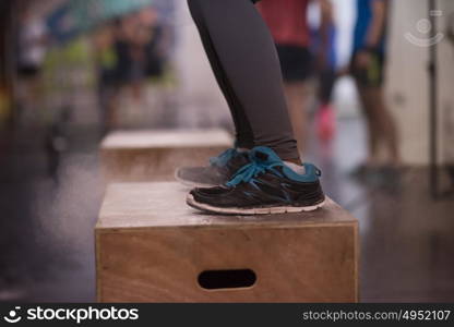 Fit young african american woman box jumping at a crossfit style gym. Female athlete is performing box jumps at gym with focus on legs