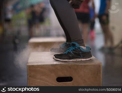 Fit young african american woman box jumping at a crossfit style gym. Female athlete is performing box jumps at gym with focus on legs