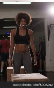 Fit young african american woman box jumping at a crossfit style gym. Female athlete is performing box jumps at gym.