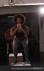 Fit young african american woman box jumping at a crossfit style gym. Female athlete is performing box jumps at gym.