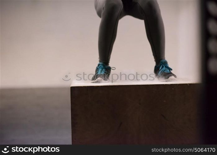 Fit young african american woman box jumping at a crossfit style gym. Female athlete is performing box jumps at gym with focus on legs