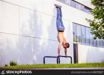 Fit young Caucasian man is doing a handstand on horizontal bar, outdoors in summer