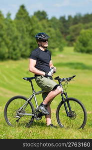 Fit young cycling man relax with water bottle in summer coutryside