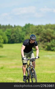 Fit young man cycling uphill mountain bike in summer coutryside