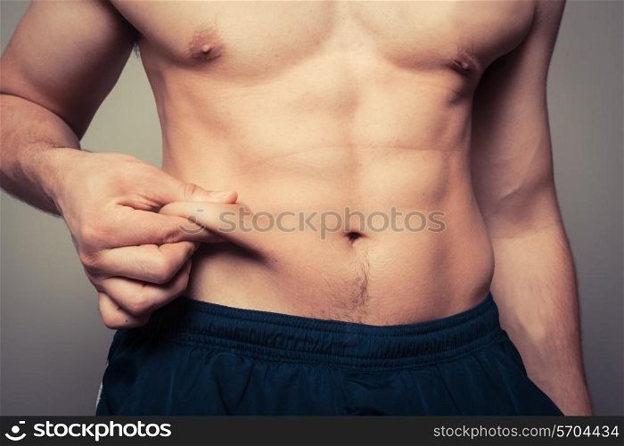 Fit young man pinching the fat on his stomach