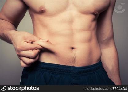 Fit young man pinching the fat on his stomach