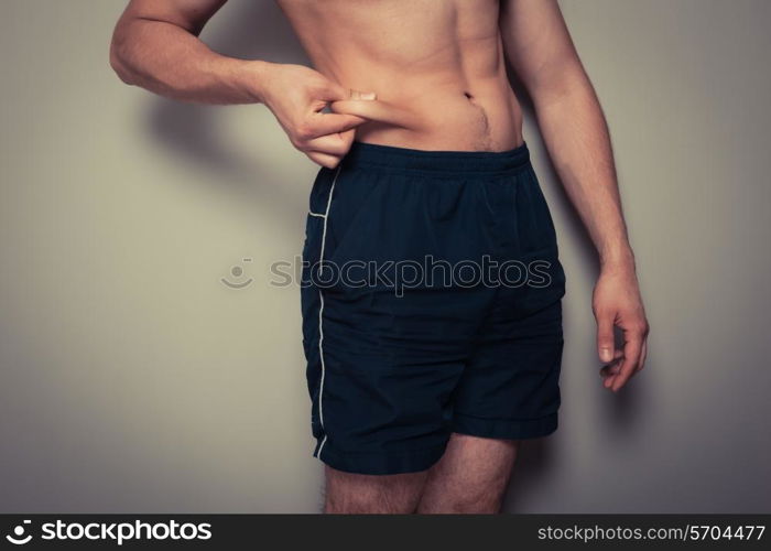 Fit young man pinching the fat on his stomach