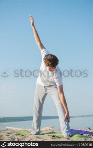 Fit young man practices yoga at the beach at morning