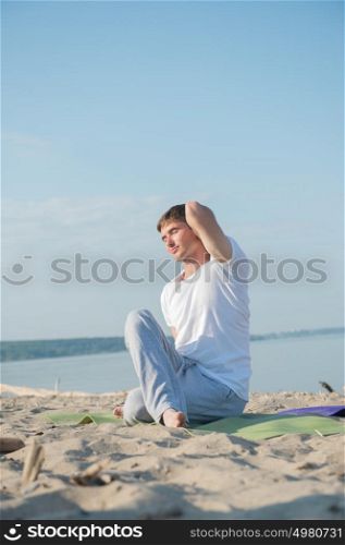 Fit young man practices yoga at the beach at morning