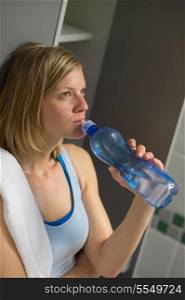 Fit young woman drinking water in locker room at gym