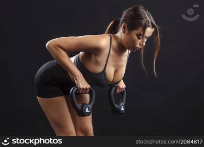 Fit young woman lifting kettle bells to exercise her upper back and arms.