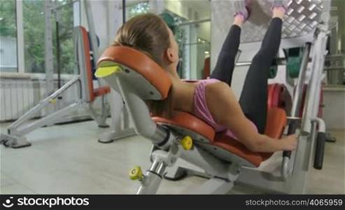Fit young woman training in health fitness club on leg press machine, closeup jib crane shot