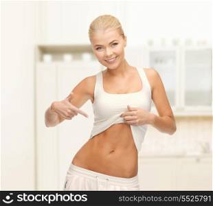 fitness and diet concept - beautiful sporty woman pointing at her abs