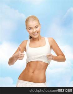 fitness and diet concept - beautiful sporty woman showing thumbs up and her abs