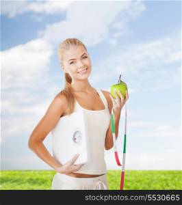 fitness and diet concept - beautiful sporty woman with scale, green apple and measuring tape