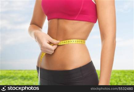 fitness and diet concept - close up of trained belly with measuring tape