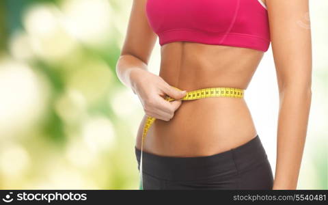 fitness and diet concept - close up of trained belly with measuring tape