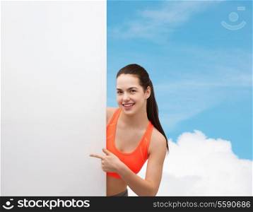 fitness and diet concept - smiling teenage girl in sportswear pointing finger to white blank board