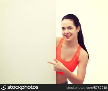 fitness and diet concept - smiling teenage girl in sportswear pointing finger to white blank board