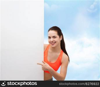 fitness and diet concept - smiling teenage girl in sportswear pointing finger to white blank board