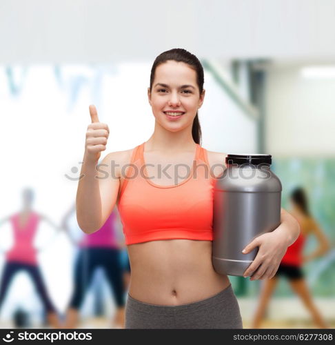 fitness and diet concept - smiling teenage girl with jar of protein showing thumbs up