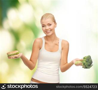 fitness and diet concept - sporty woman with broccoli and hamburger