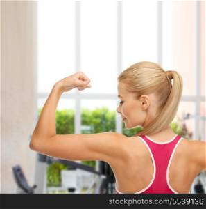 fitness and gym concept - young sporty woman showing her biceps