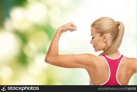 fitness and healtcare concept - young sporty woman showing her biceps