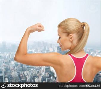 fitness and healthcare concept - young sporty woman showing her biceps