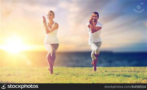 fitness and people concept - couple making yoga eagle pose outdoors over sea background. couple making yoga eagle pose outdoors