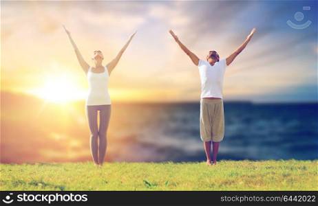 fitness and people concept - couple making yoga exercises outdoors over sea background. couple making yoga exercises outdoors