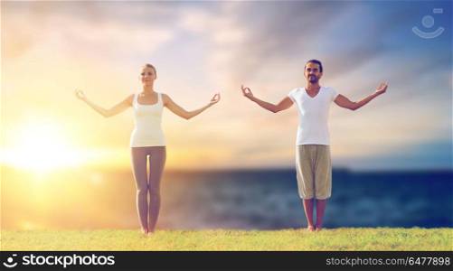 fitness and people concept - couple making yoga exercises outdoors over sea background. couple making yoga exercises outdoors. couple making yoga exercises outdoors
