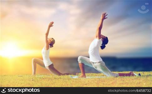 fitness and people concept - couple making yoga low lunge pose outdoors over sea background. couple making yoga low lunge pose outdoors