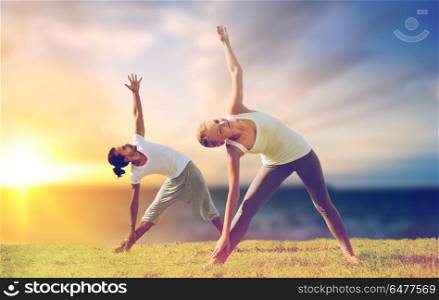 fitness and people concept - couple making yoga triangle pose outdoors over sea background. couple making yoga triangle pose outdoors. couple making yoga triangle pose outdoors