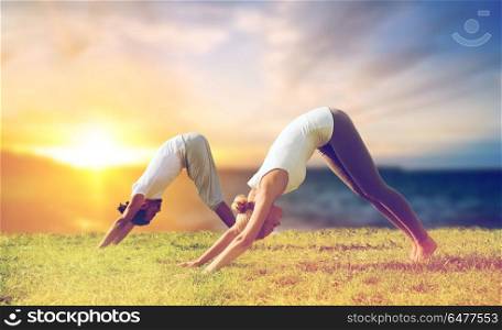 fitness and people concept - smiling couple making yoga downward facing dog pose outdoors over sea background. smiling couple making yoga dog pose outdoors. smiling couple making yoga dog pose outdoors