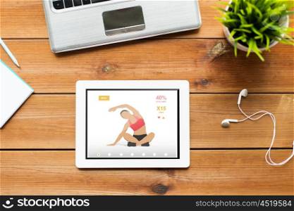 fitness and technology concept - close up of tablet pc computer, laptop and earphones on wooden table with sport application on screen