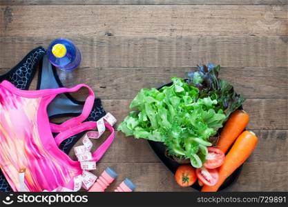 Fitness and weight loss concept. Woman's sport bra and healthy foods on wooden background with copyspace