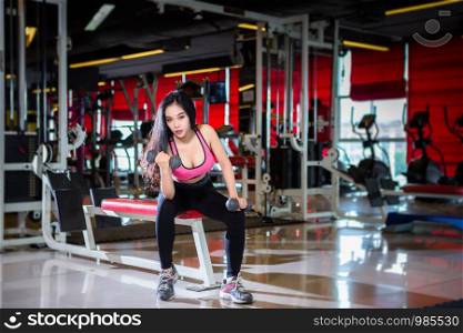 Fitness Asian women performing doing exercises training with dumbbell sport in sport gym interior and fitness health club with sports exercise equipment Gym background.