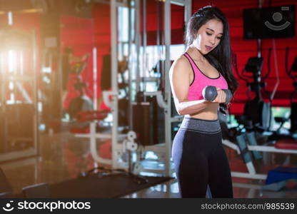 Fitness Asian women performing doing exercises training with dumbbell sport in sport gym interior and fitness health club with sports exercise equipment Gym background.