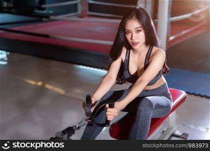 Fitness Asian women performing doing exercises training with rowing machine (Seat Cable Rows Machine) in sport gym interior and fitness health club with sports exercise equipment Gym background.