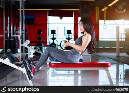 Fitness Asian women performing doing exercises training with rowing machine (Seat Cable Rows Machine) in sport gym interior and fitness health club with sports exercise equipment Gym background.