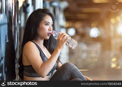 Fitness Asian women sitting in sport gym interior and fitness health club with a bottle of water.