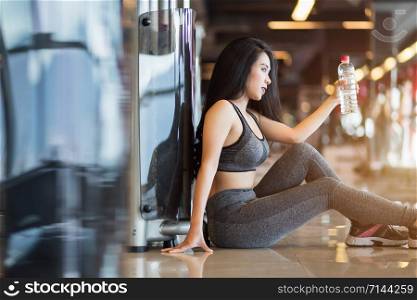 Fitness Asian women sitting in sport gym interior and fitness health club with a bottle of water.