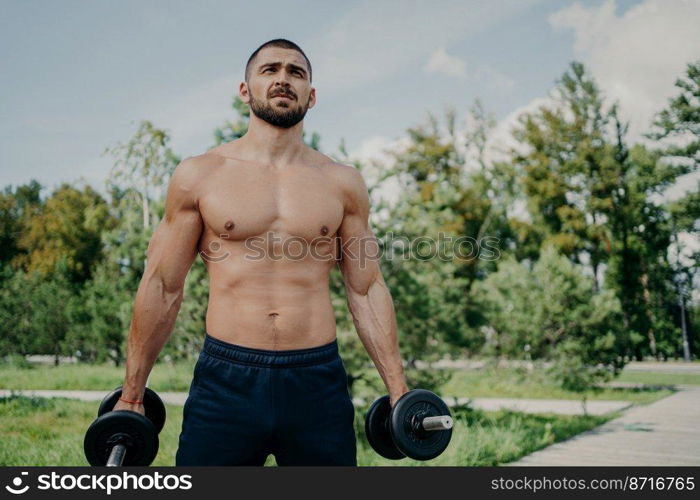 Fitness athlete muscular man holds barbells in hands, has naked perfect body, strong arms and biceps, doing exercises outdoor, trains muscles and triceps. Weightlifting and endurance concept