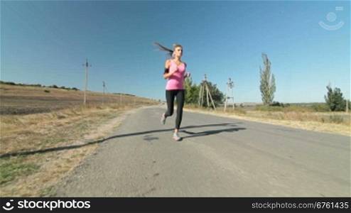 Fitness athletic girl jogging along the road during outdoor workout wide angle