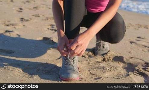 Fitness athletic girl lacing sport shoes before start jogging on the beach close-up