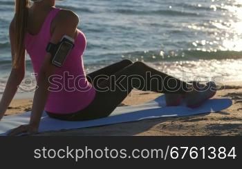 Fitness athletic girl relaxing after exercise on the beach at sunset