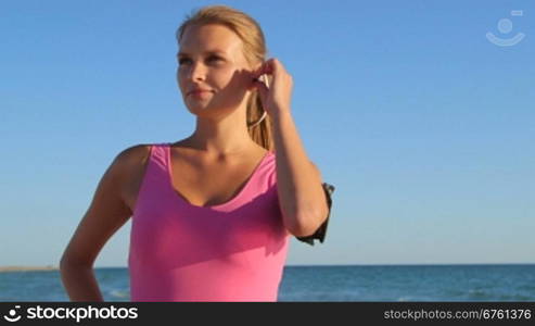 Fitness athletic girl using sport wireless headset while exercising on the beach medium shot