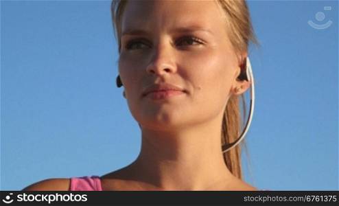 Fitness athletic girl using sport wireless headset while exercising outdoors close-up