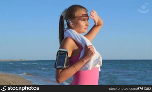 Fitness athletic girl with wireless headset and smart phone in sport armband during workout on the beach